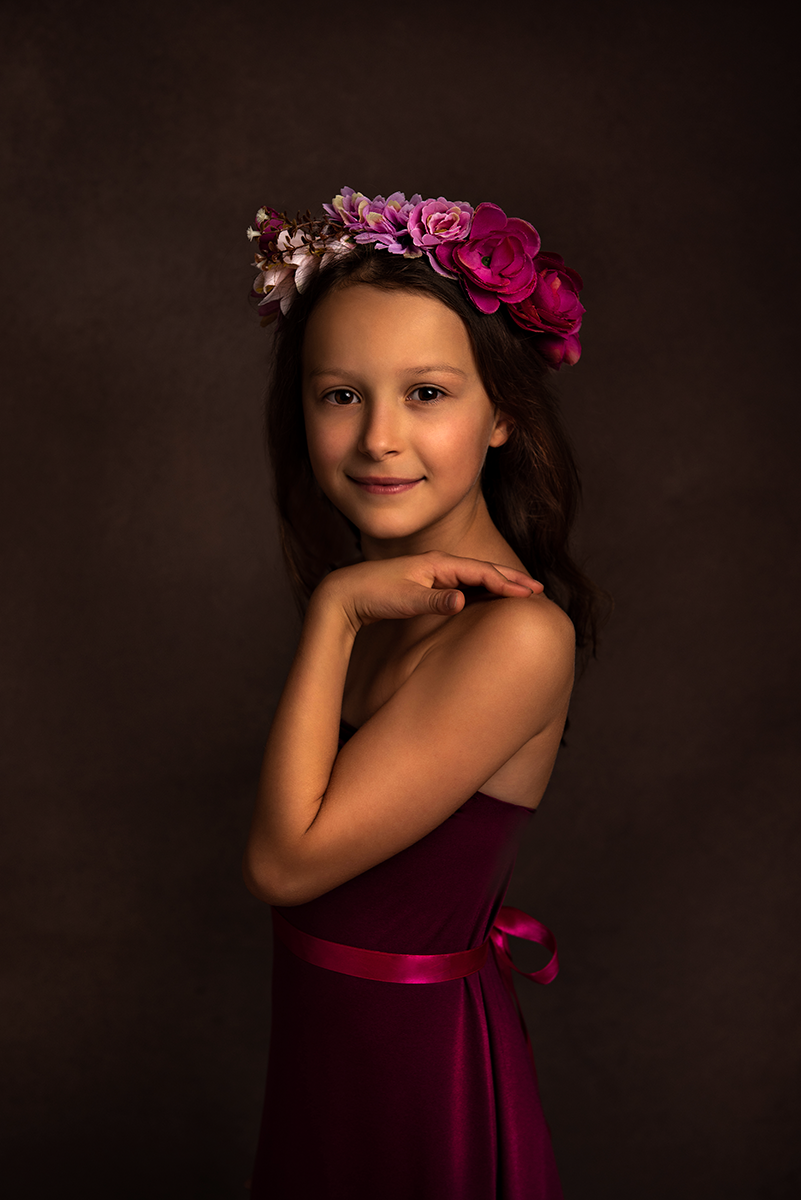 Ritratto meravigliosa bambina con coroncina floreale e vestito in velluto viola su sfondo nero
