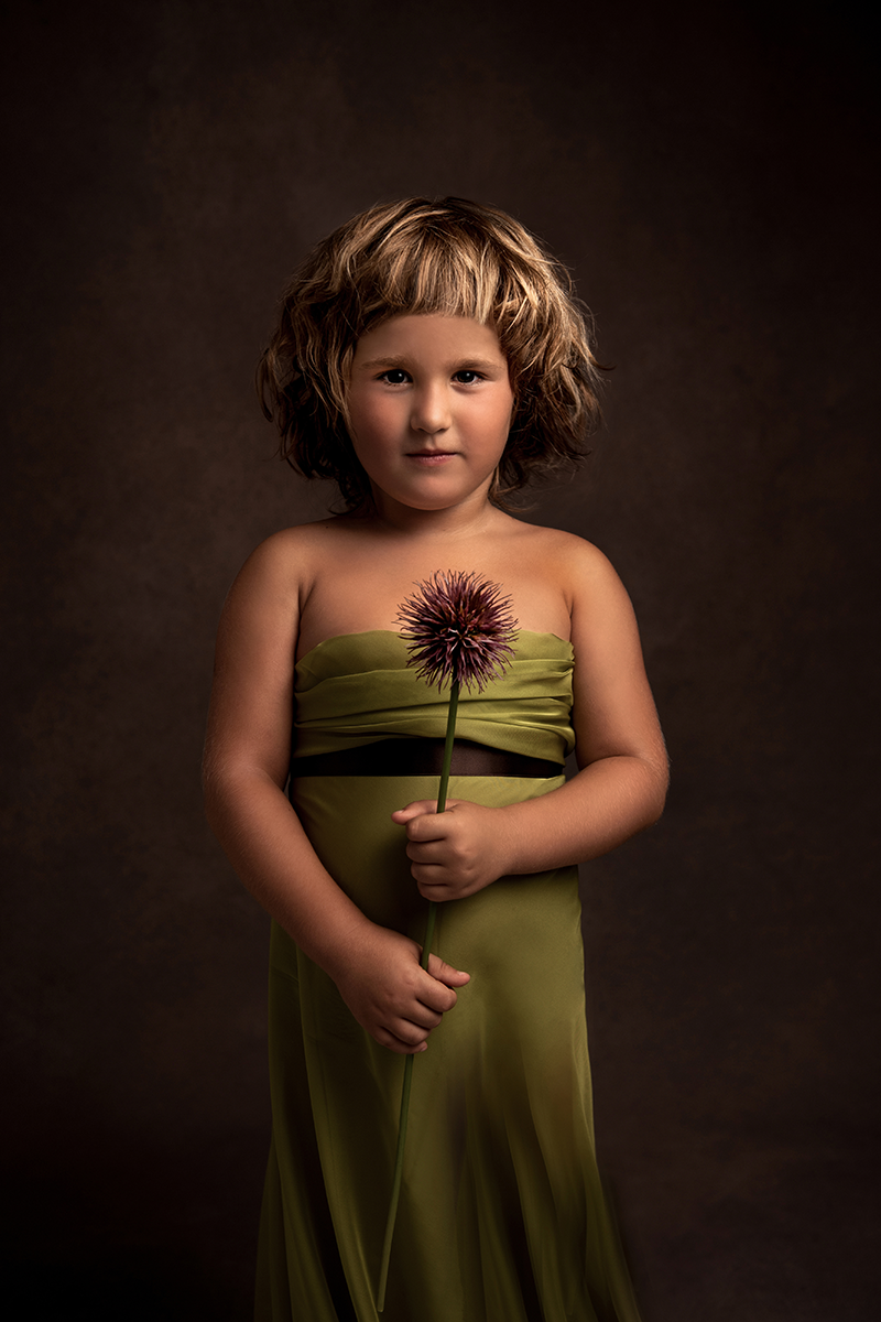 Ritratto bellissima bambina con vestito a fascia verde con fiore in mano
